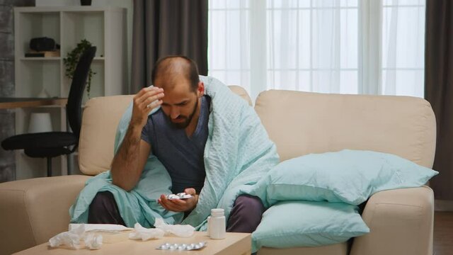 Sad and sick man on sofa wrapped with blanket during global pandemic.