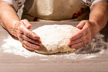 Baker hands making dough on wooden board in kitchen. Woman great-grandmother kneads dough for home...