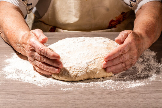 Baker hands making dough on wooden board in kitchen. Woman great-grandmother kneads dough for home baking