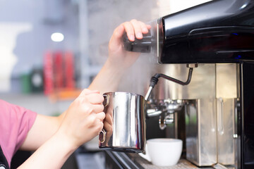 Fototapeta na wymiar Coffee shop worker preparing coffee on steam espresso coffee machine. Barista Warming Milk In Metal Jug With Steam Of Coffee Machine