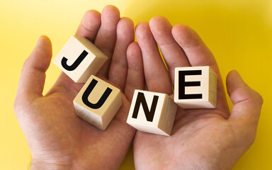 Men's hands are holding wooden blocks with the text June on a yellow background