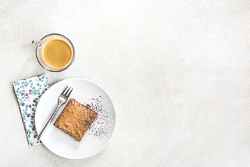 Top view of a cup of coffee and a dessert plate with brownie cake over white rustic background.