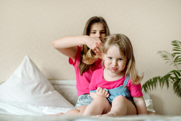 Fototapeta na wymiar cute sister teen combing hair baby in bed.Cute girls are laughing and smiling. Morning treatments, hair care, care. Family love. Cozy bright bedroom.