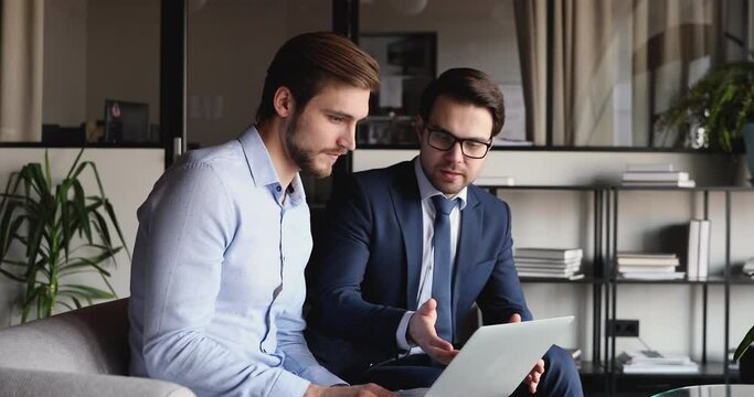 Two happy businessmen using laptop shake hands in office express trust, gratitude for good financial results. Manager and client handshaking making agreement in providing internet business services.