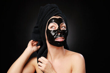 Close up view of caucasian adult woman relaxing with black peel off mask and dark blue towel covering hair isolated on black background. Spa concept.