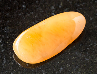 closeup of sample of natural mineral from geological collection - tumbled yellow chalcedony rock on black granite background from India