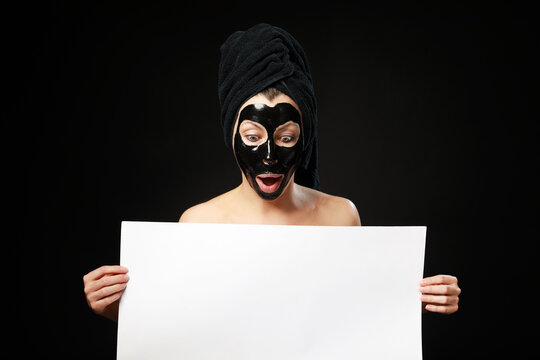 relaxing with black peel off mask and holding  clear white paper with copy space for text isolated on black background.