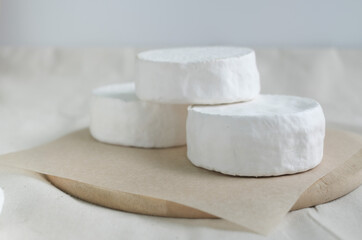 Homemade cheese on wooden plate at light background.