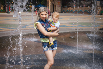 nice mother walks with her son in amusement park, happy woman with her son in her arms looks at the fountain