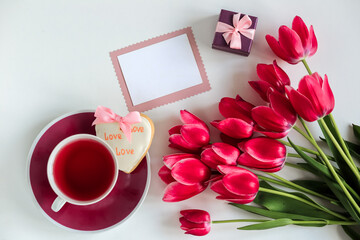A bouquet of delicate pink tulips with gifts on a white background with a Cup of tea and a gingerbread. Holiday concept, Greetings on international women's day