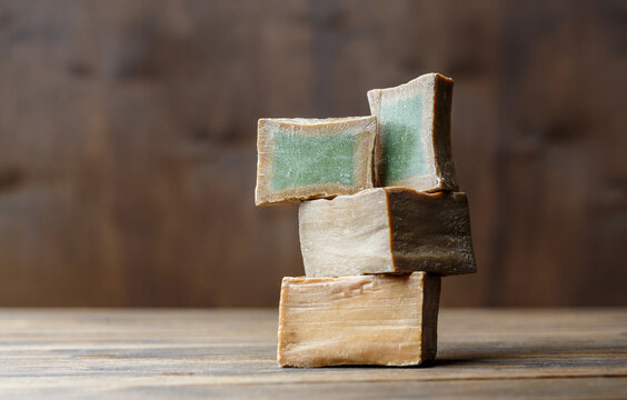 Two bars and slices of traditional aleppo organic laurel soap on a brown wooden background.