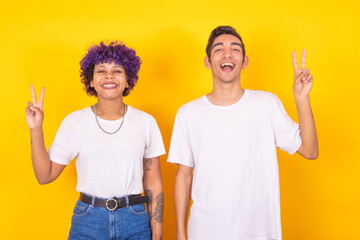 smiling young people celebrating with victory sign isolated on color background
