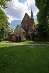 Fototapeta na wymiar Part of the Luebeck cathedral with narthex and ridge turret, view from the idyllic churchyard with lawn and old trees, copy space