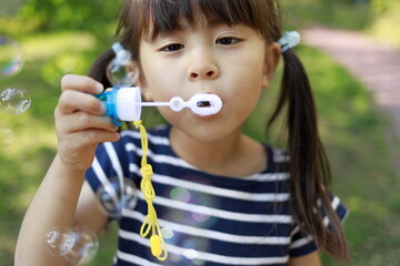 緑の中でシャボン玉で遊ぶ幼児(5歳児)