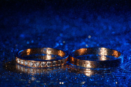 Wedding Rings With Water Drops On A Dark Blue Neon Backlight Background.