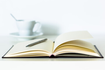 Open notebook with pen and coffee mug in the background. Writing book and morning study.