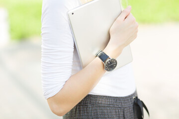 Closeup crop of student girls arm wearing a watch and carrying a digital touch screen tablet computer while walking outdoors. 