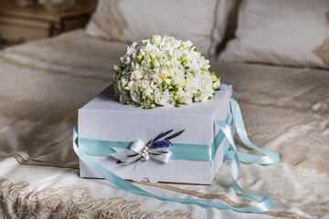 
A bride's bouquet of white roses and white azaleas lies on a beautiful packing box on a wedding day on a vintage bed.