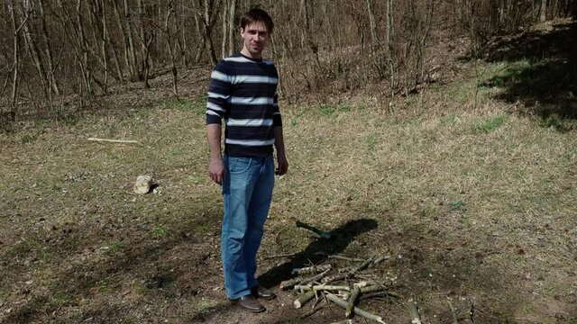 Caucasian man throws an ax into the ground and sticks it into the grass, then he comes up and picks up the instrument