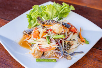 Papaya salad with fresh blue swimming crab, put papaya in a white plate on a brown table in a restaurant