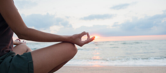 Young woman practicing yoga outdoors. Girl meditating with sunset sea view at background, panoramic banner. Harmony, meditation, relaxation, healthy lifestyle concept.