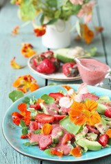 salad with nasturtium flowers and leaves with strawberries and avocados. dressed with strawberry vinaigrette or strawberry dressing with poppy seeds.