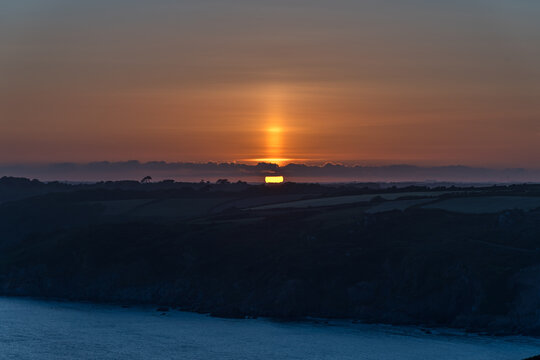 The glow of the setting sun behind low cloud at Dodman Point, Cornwall in late Spring
