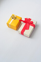 Two gift boxes with bows white with a red ribbon in white peas and yellow with a gold ribbon stand next to each other on a white.