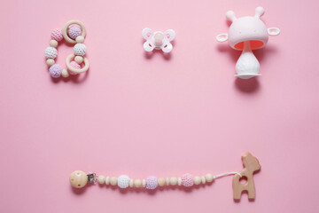 Baby accessories concept: teether, caterpillar toy and baby pacifier, over pink background with copy space, top view, flat lay.