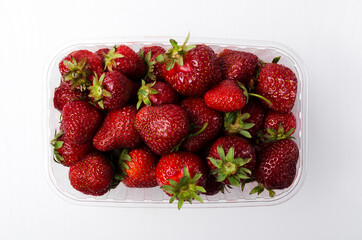 Top view of fresh juicy strawberries in the plastic container, white background