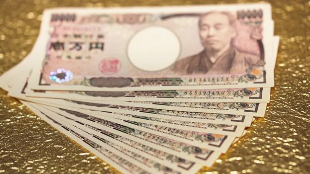 Close-up rack focus video of 100,000 yen in cash sent by the Japanese govt of Abe Shinzo to fight economic unemployment crisis caused by COVID-19 on a golden background.