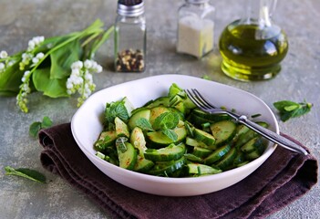 Fresh salad of cucumbers, green onions and fresh mint in an clay plate on a gray concrete background. Cucumber recipes. Vegetable salads, vegan food. Healthly food.