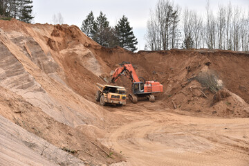 Excavator load the sand to the heavy mining truck in the open-pit. Heavy machinery working in the mining quarry. Digging and excavation operations. View on the mountains with yellow sand
