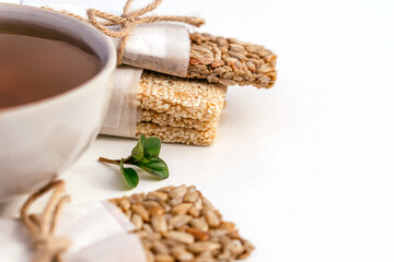 Cup of tea and homemade kozinaki from sunflower seeds, sesame on Jerusalem artichoke syrup on white background.Сoncept of healthy food and healthy desserts.Selective focus with shallow depth of field