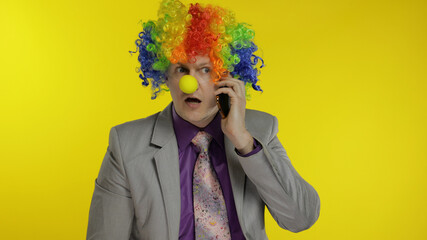 Clown businessman entrepreneur boss talking on mobile phone. Yellow background