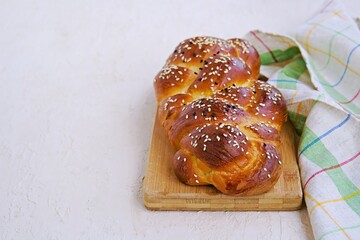 Homemade sliced challah, traditional wicker white bread on a wooden board on a light concrete background. Copyspace.