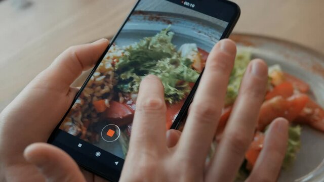 Closeup of a woman using a smartphone camera shoots a vegetable salad on a plate
