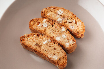 Popular Italian Biscotti or Cantucci biscuit cookies stuffed with nuts on brown plate with copy space.
