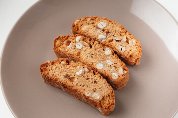 Popular Italian Biscotti or Cantucci biscuit cookies stuffed with nuts on brown plate with copy space.
