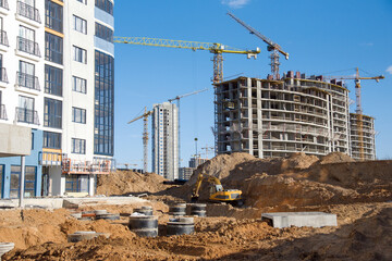 Excavator on earthworks for laying heating pipes and stormwater in trench. Installing concrete wells, сhambers, manholes near new multi-storey residential building. Tower cranes at construction site