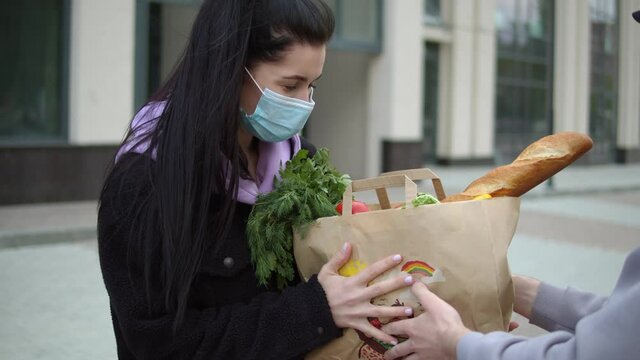 Portrait of delivery man wearing cap and medical mask carrying packet with fresh food. Order products online stay at home Courier bringing grocery to house, door to door delivery during quarantine. 