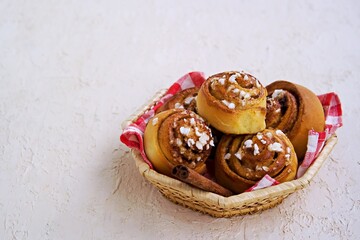 Swedish twisted cinnamon rolls sprinkled with pearl sugar in a wicker basket on a light concrete background. Cinnamon pastry