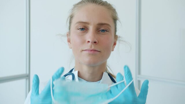 Portrait of female doctor pretty young blonde taking off facial mask breathing and smiling standing alone in clinic during global epidemic of corona virus.