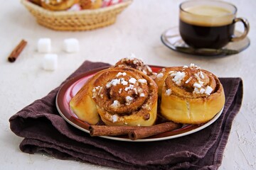 Swedish twisted cinnamon rolls sprinkled with pearl sugar on a red plate on a light concrete background. Cinnamon pastry