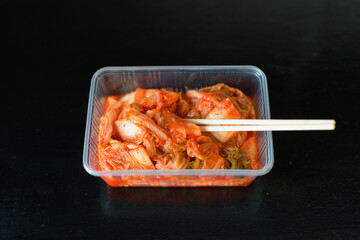 Traditional Korean Food Kimchi Served in Plastic Container With Chopsticks Horizontal Shot Against Black Background