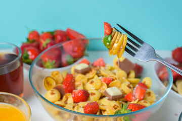 tiny pancakes on a fork with fresh strawberries, banana, chocolate, coconut chips and honey in a plate on a blue background. food trend 2020