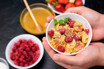 mini pancake cereal bowl with fresh strawberries banana chocolate, coconut shavings and honey in small plates. the view from the top . the trend of self-isolation