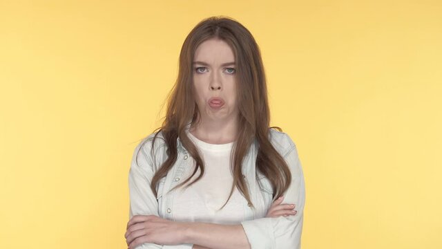 Portrait of unhappy young woman showing tonque. yellow background.