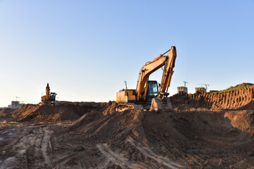 Obraz premium Excavators working at construction site on earthworks. Backhoe digging building foundation. Paving out sewer line. Construction machinery for excavating, loading, lifting and hauling of cargo