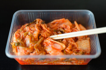 Close-up Shot Of Traditional Korean Food Kimchi Served in Plastic Container With Chopsticks Horizontal Shot Against Black Background